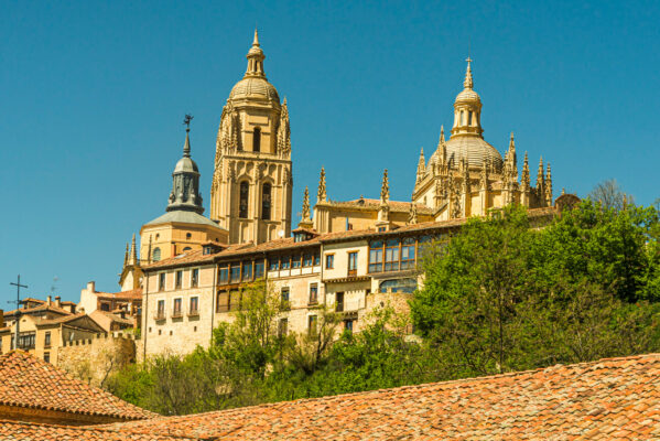 Sunny cityscape of Segovia Cathedral’s dome and bell tower rising above ochre rooftops in Spain.