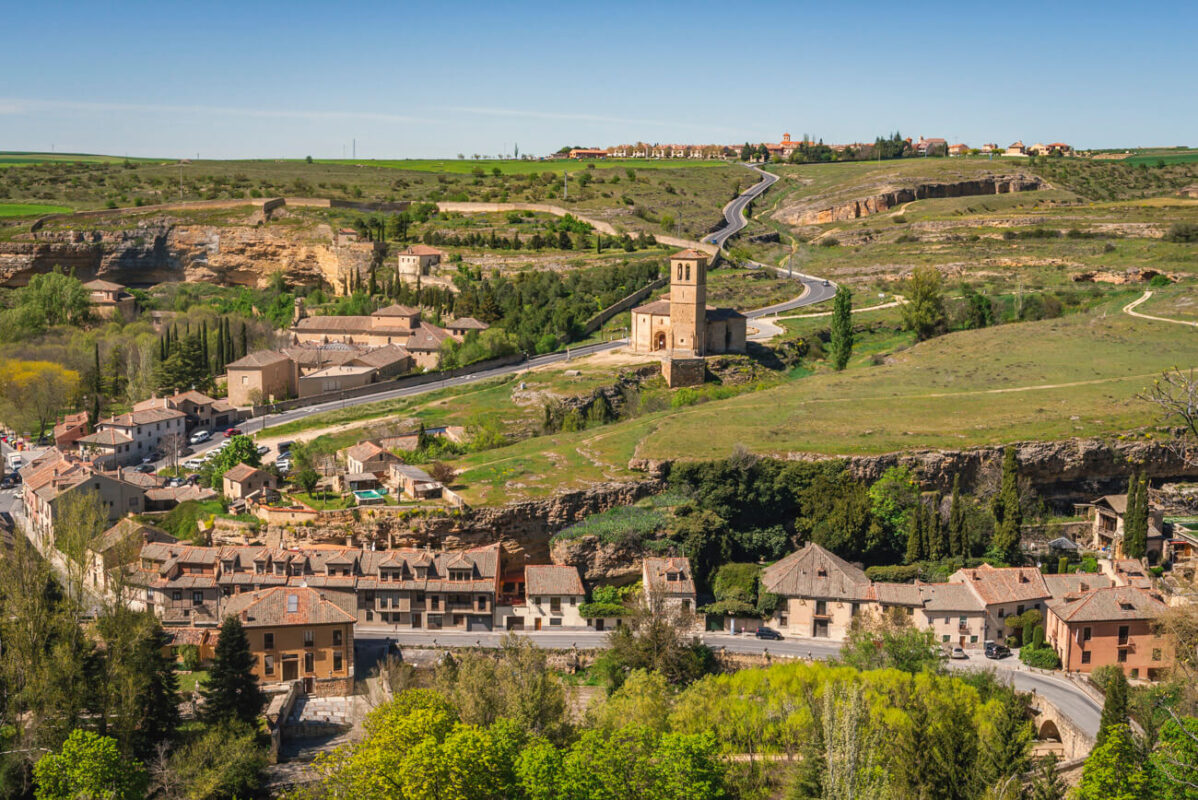 Panoramic view of Iglesia de la Vera Cruz in Segovia, Spain - Romanesque church amid green landscape and a winding road.
