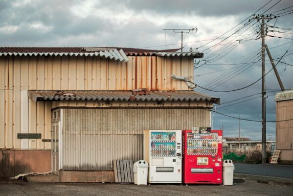 Red and white Japanese vending machines outside a weathered building at Nakaminato Port in Ibaraki, Japan.
