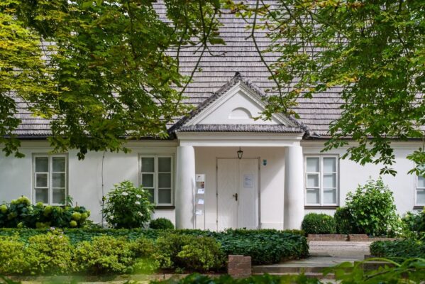 Fryderyk Chopin's white birthplace house in Zelazowa Wola, framed by leafy trees and a lush summer garden.